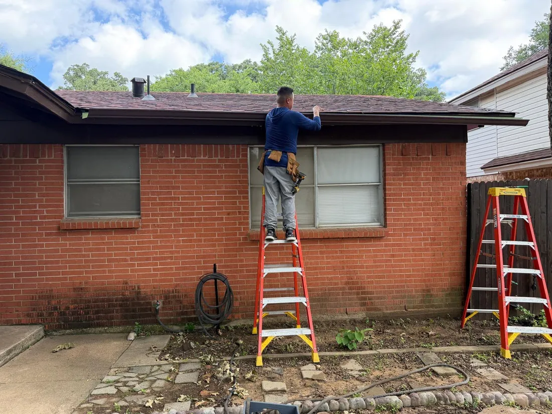 Technician installing new gutters on a brick home Dallas TX
